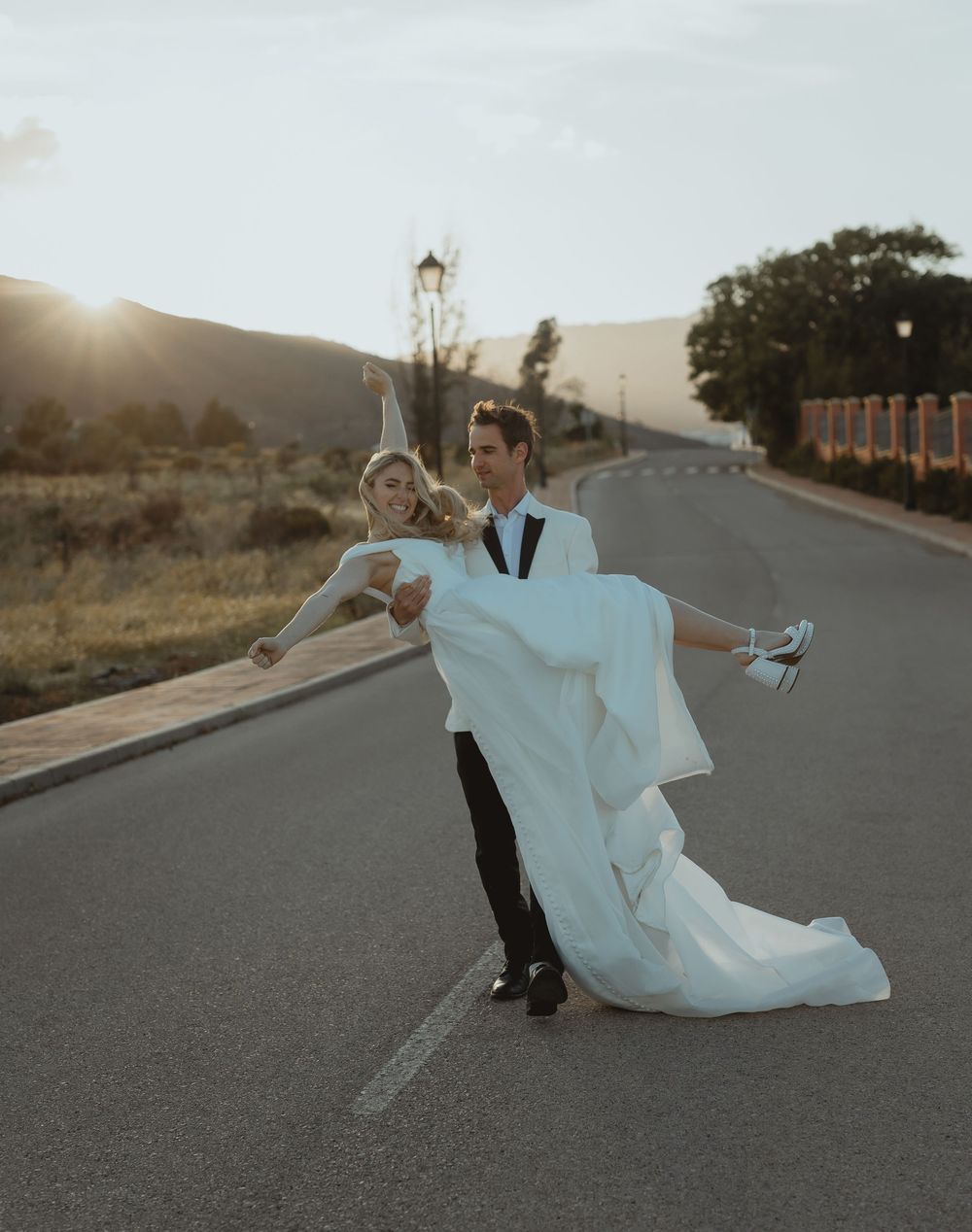 Newlyweds playfully pose on an empty road at dusk with flowing white wedding dress.