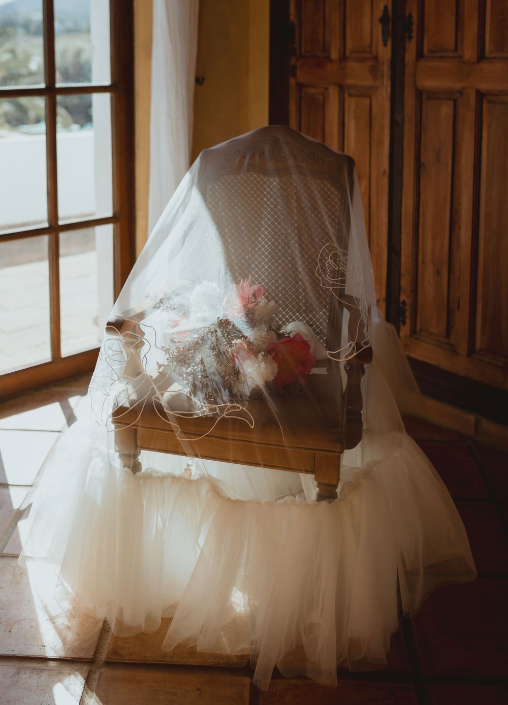 White tulle wedding dress skirts hanging in golden sunlight streaming through wooden windows, creating dreamy ambiance.