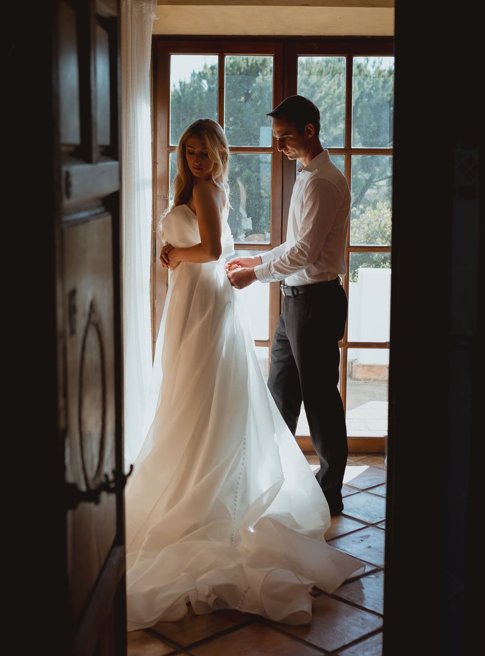A quiet indoor scene shows wedding preparations with flowing white dress details and window light creating a soft atmosphere.
