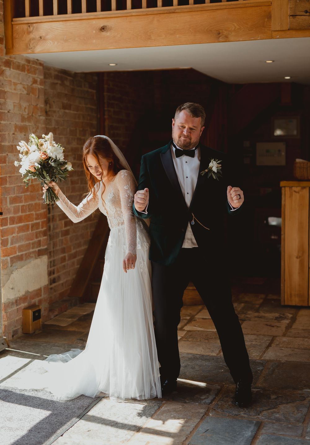 Wedding couple poses in romantic lighting against rustic brick wall interior at elegant indoor venue.