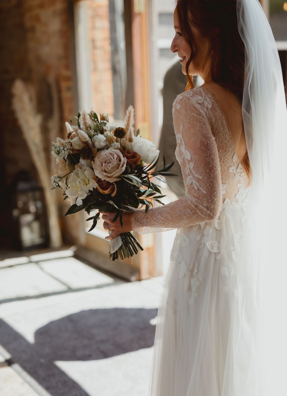 Elegant bridal bouquet held against flowing white wedding dress with brick backdrop in natural lighting.