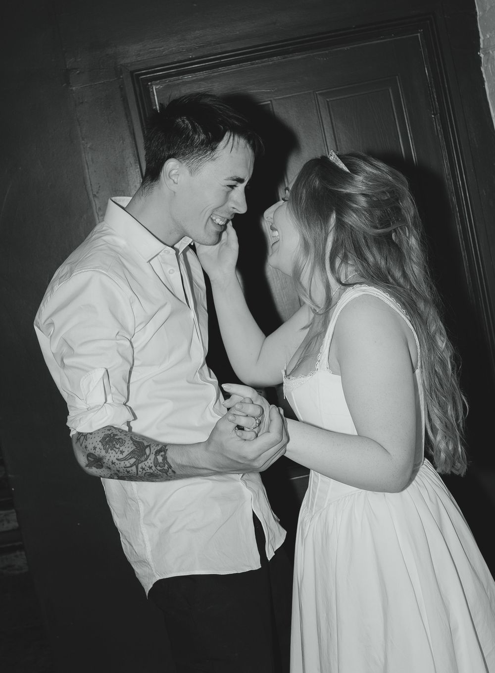Black and white photo of a smiling couple dancing together, the woman in a white dress touching the mans face.