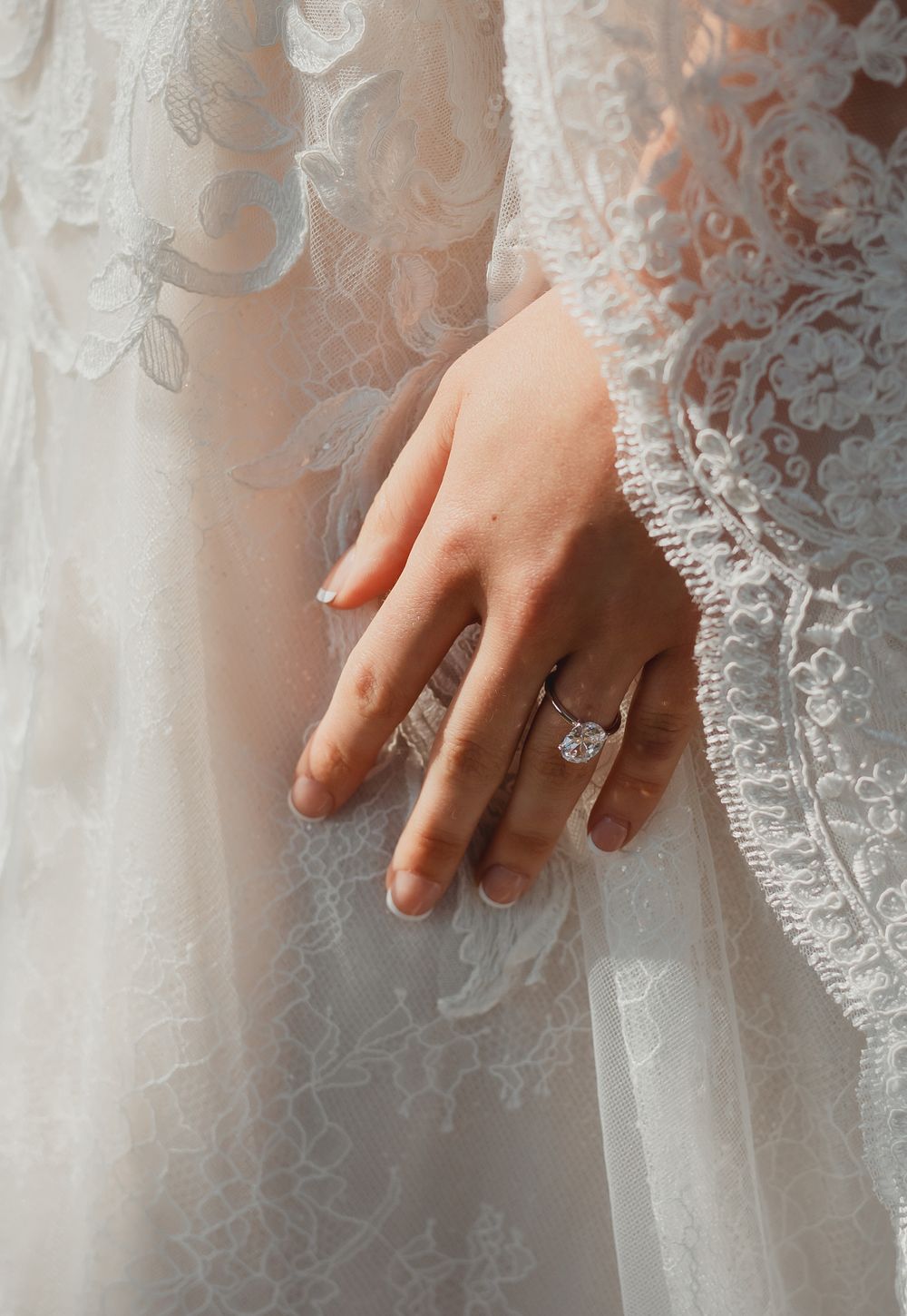 A delicate lace wedding dress detail is shown with a close-up of hands gracefully touching the fabric.
