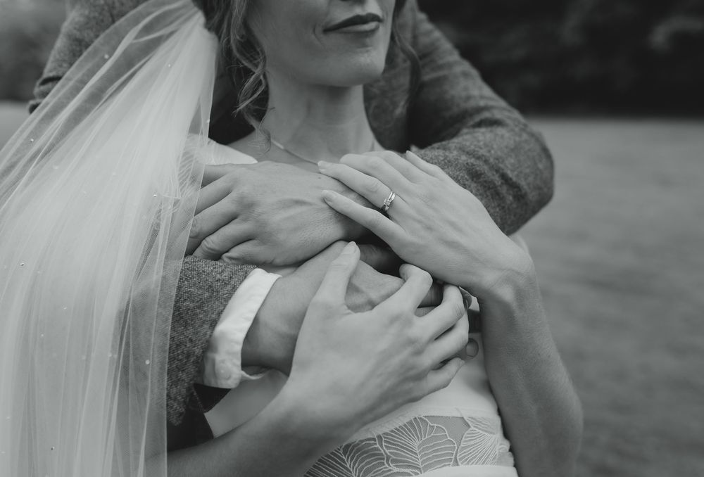 Black and white wedding photo of bride and groom embracing, showing hands and veil details.
