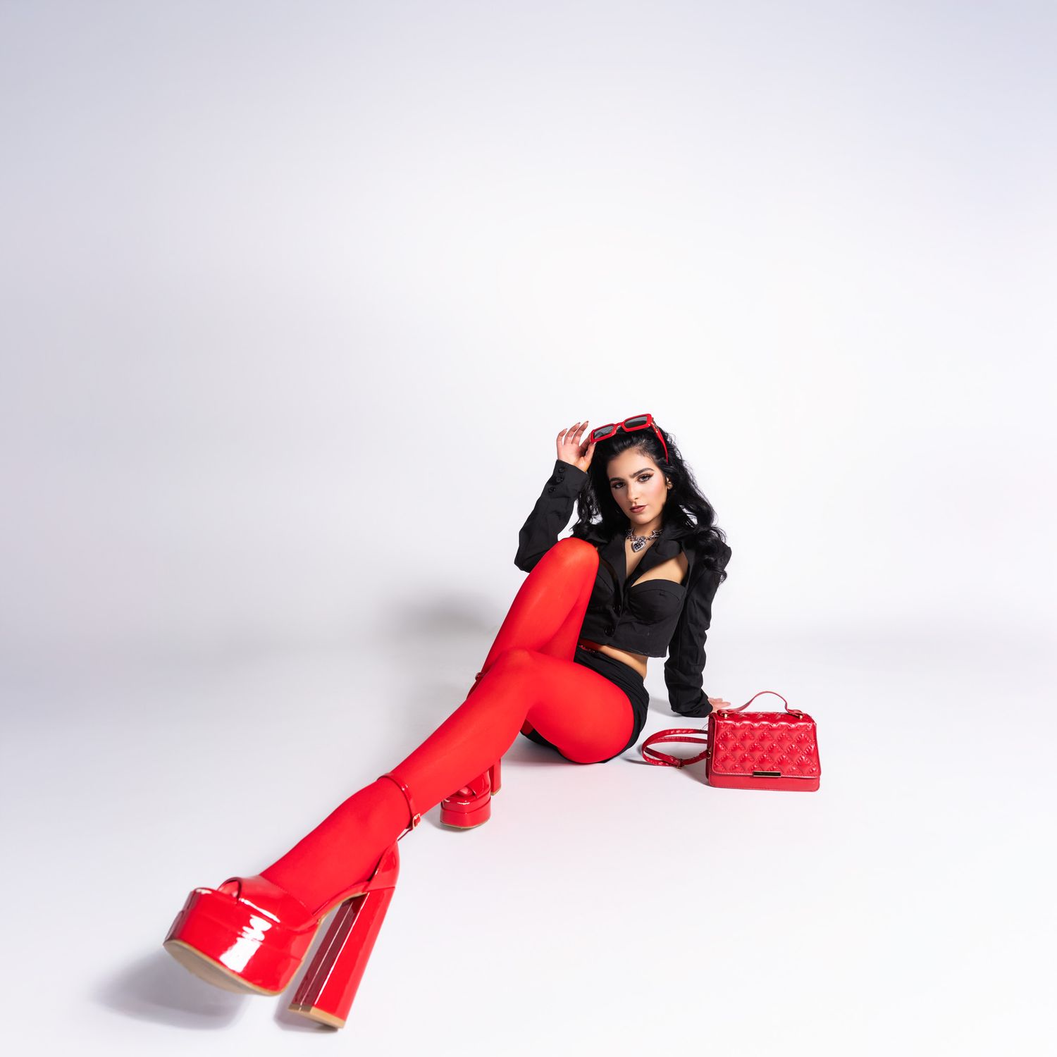 Person in retro-inspired outfit with red bell bottom pants and black top poses with red handbag against light background.