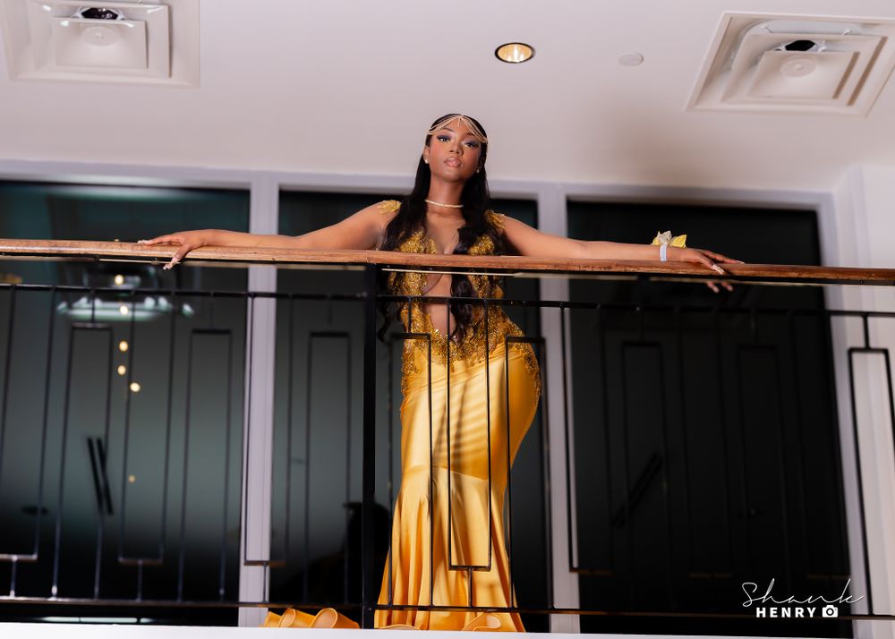 Dramatic pose on balcony railing in flowing gold evening gown with train.