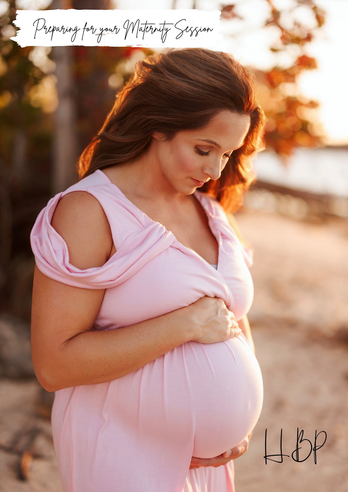 Pregnant woman in pink dress cradling baby bump during golden hour maternity photography session outdoors.