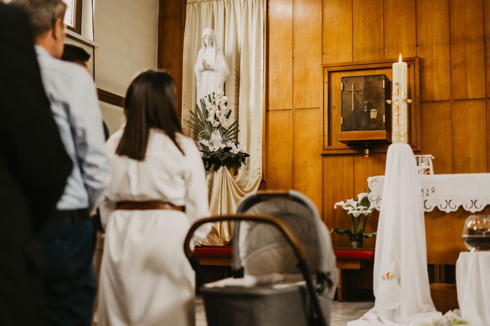 Interior of a church decorated with white flowers and a cross for a baptismal ceremony.