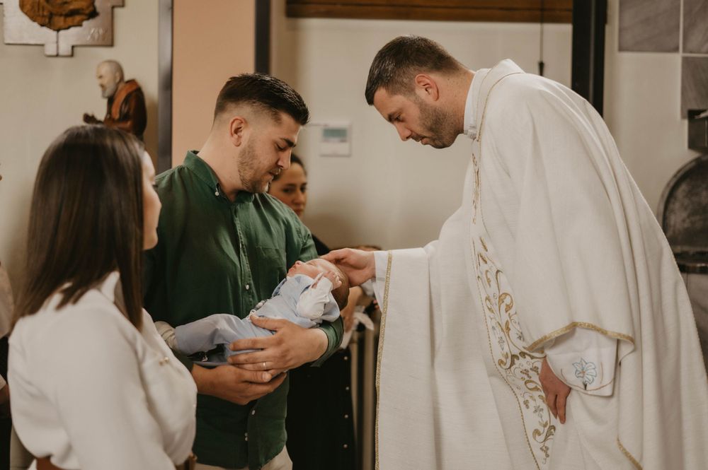 A religious ceremony taking place with a priest in white robes blessing an infant.