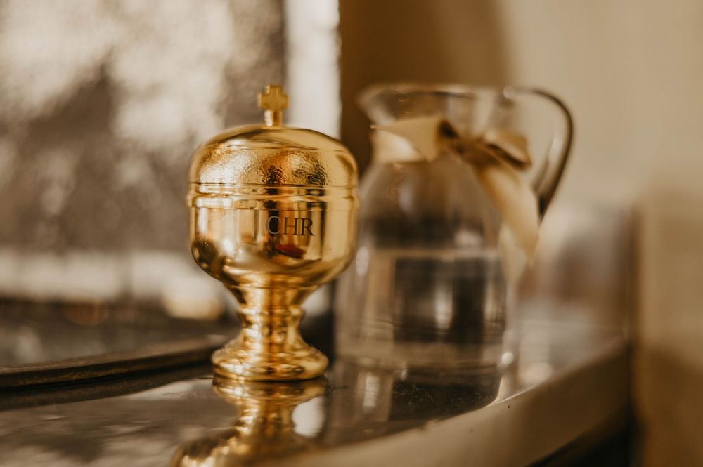 Golden ceremonial vessel for holy water sitting beside glass container.