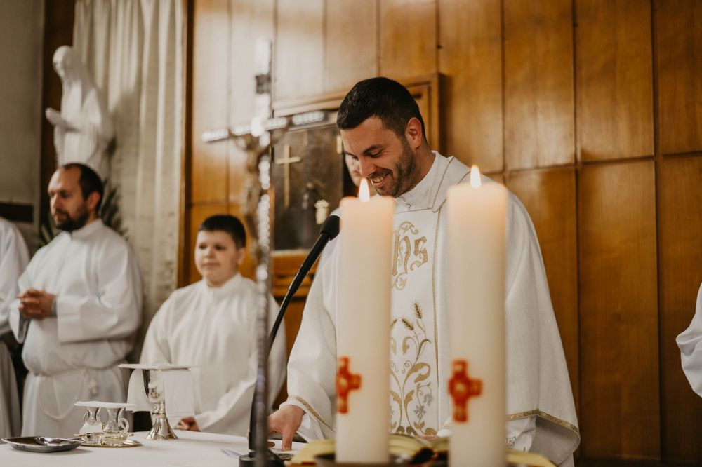Priest wearing white ceremonial robes with red cross embellishments during a church service.