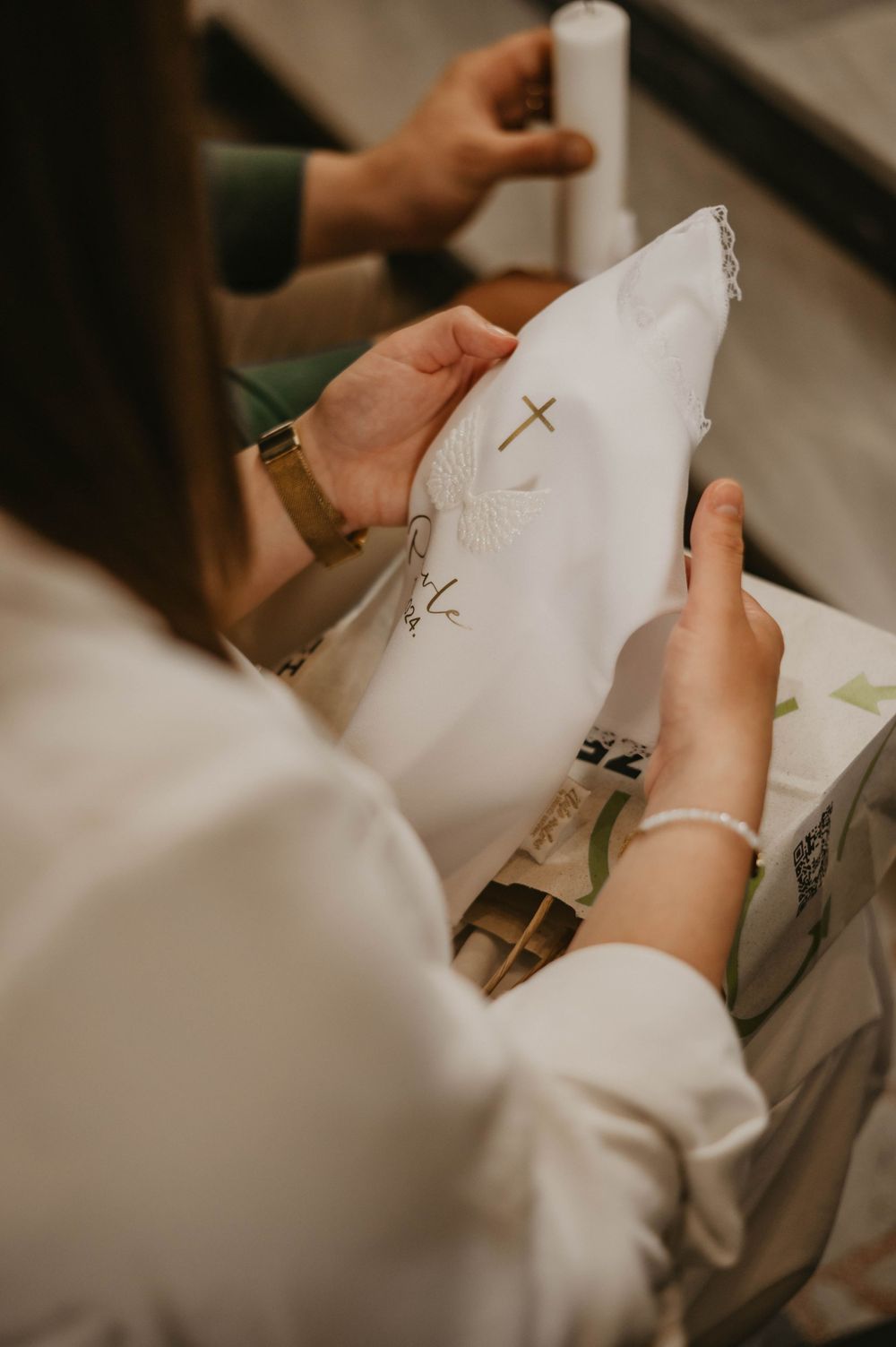 Hands holding white fabric with embroidered cross designs during a religious ceremony preparation.