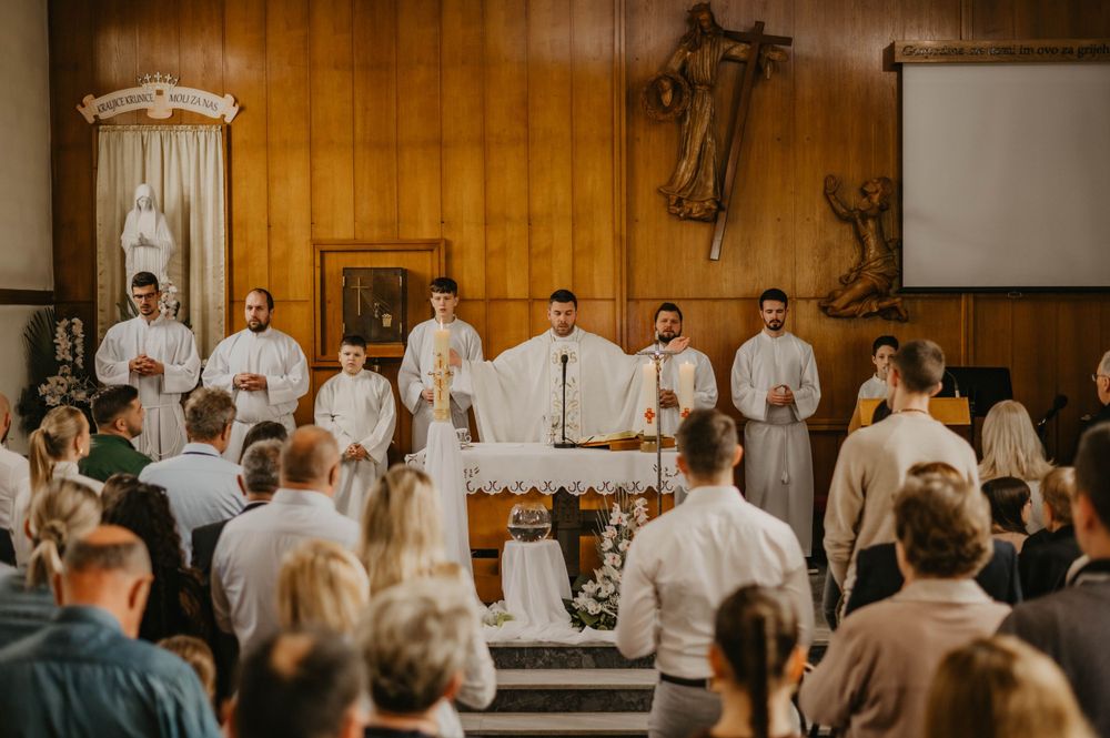Church service with white-robed clergy and congregation in a wood-paneled sanctuary.