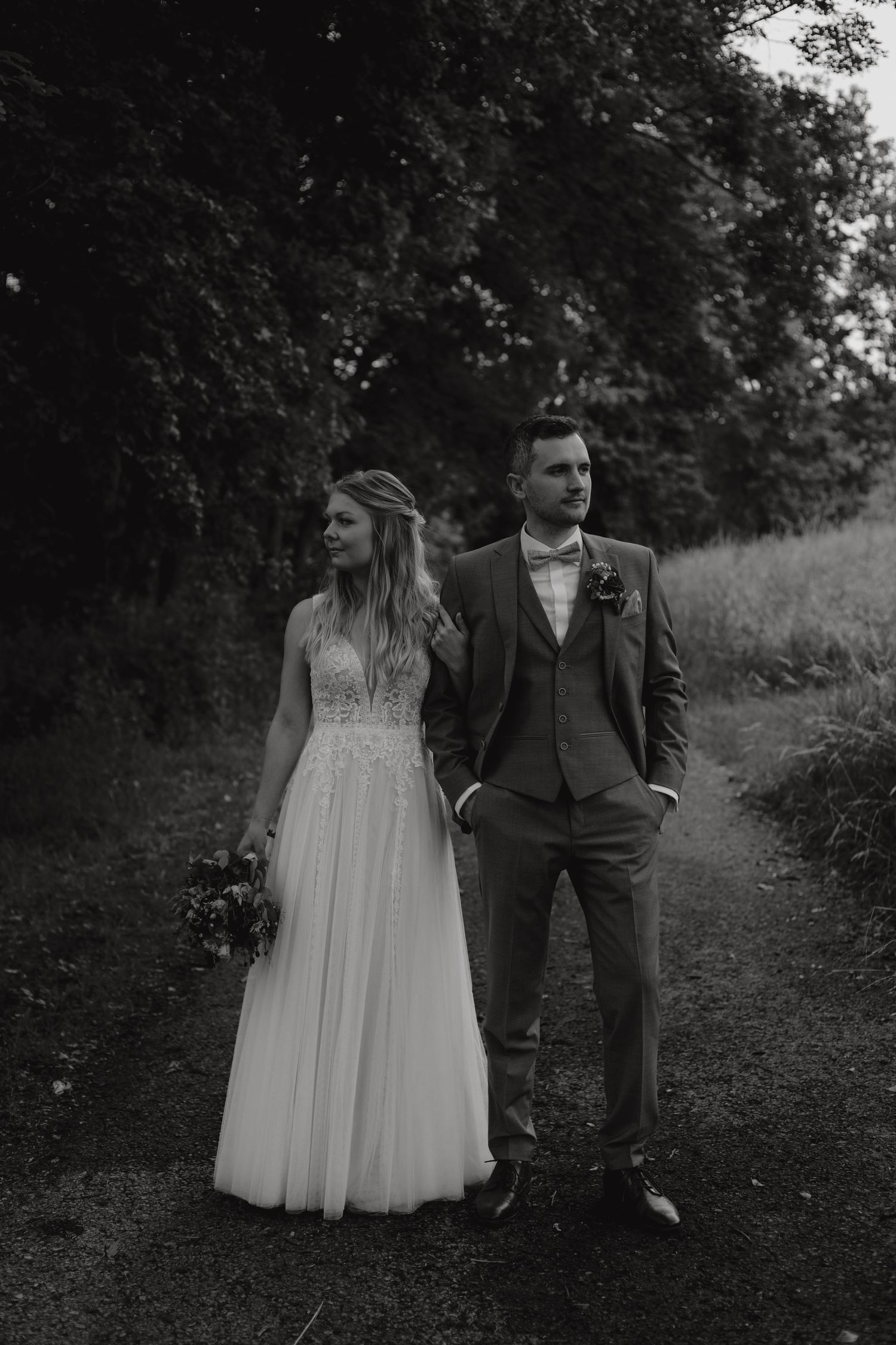 Black and white portrait of newlyweds standing on woodland path.