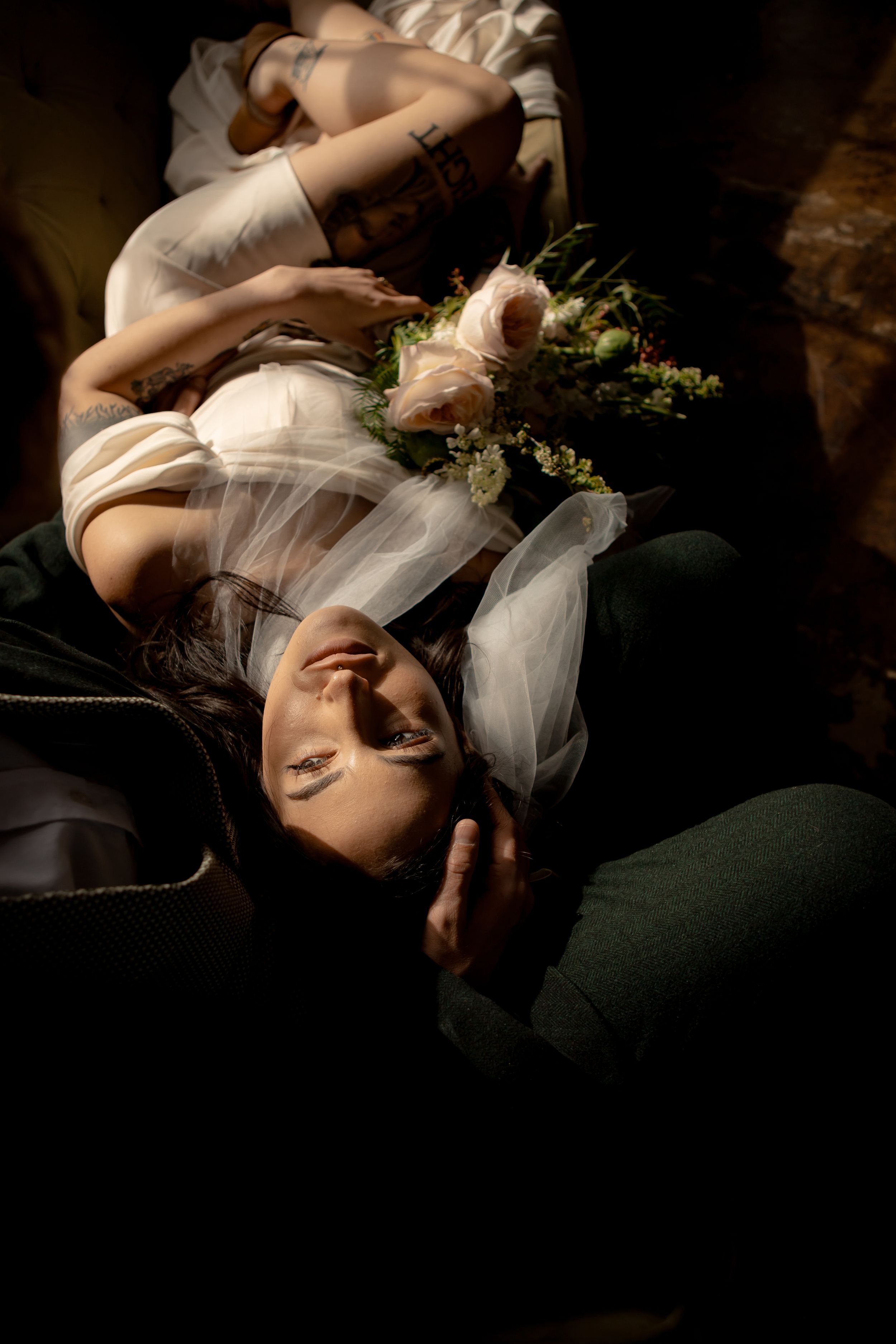 Dramatic portrait of person in white dress with roses in moody lighting.