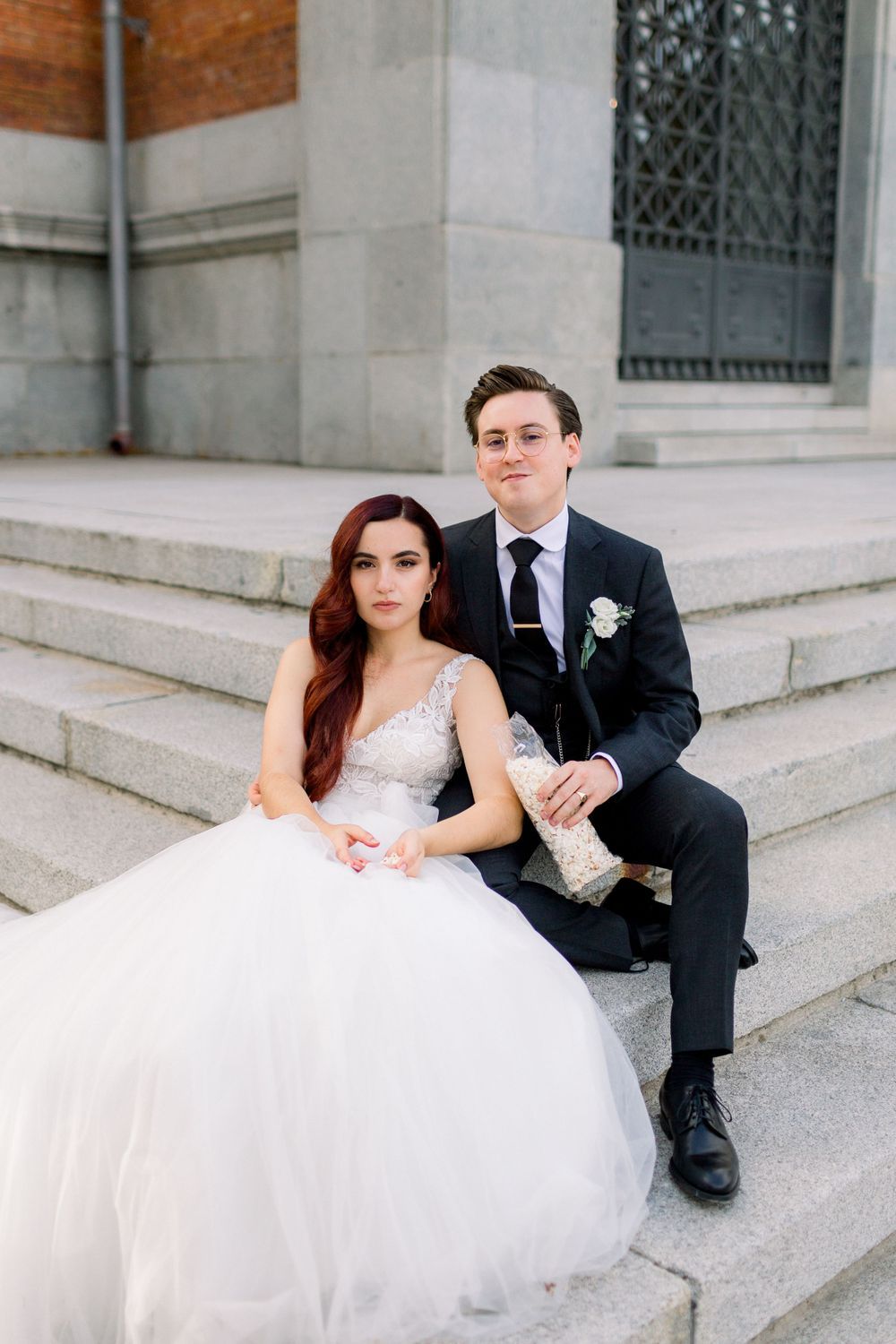 Una pareja vestida de boda se sienta junta en los grandes escalones de piedra de un edificio histórico.