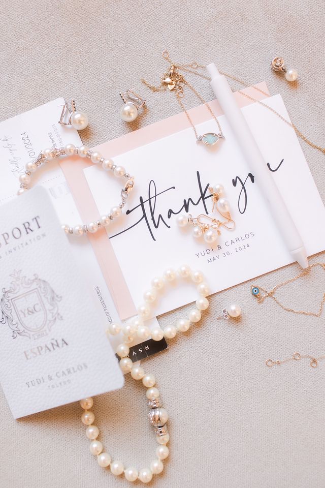 Wedding thank you note surrounded by delicate pearl jewelry and accessories on beige background.