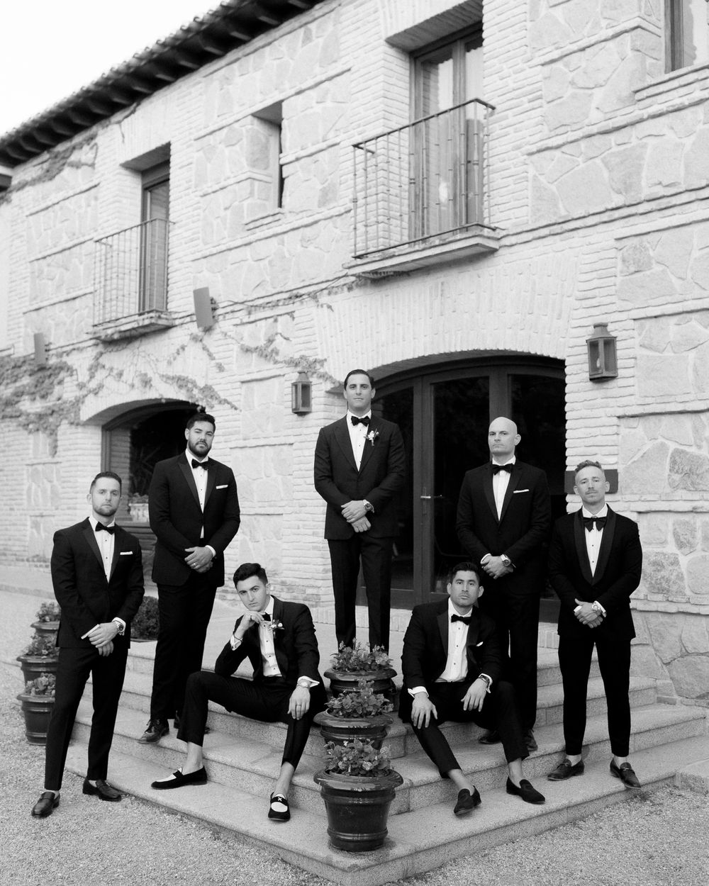 Black and white portrait of groomsmen posing in formal attire outside a stone building.