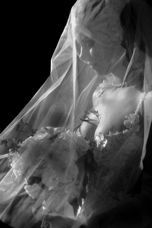 Dramatic black and white portrait of a bride in a flowing veil and lace dress.