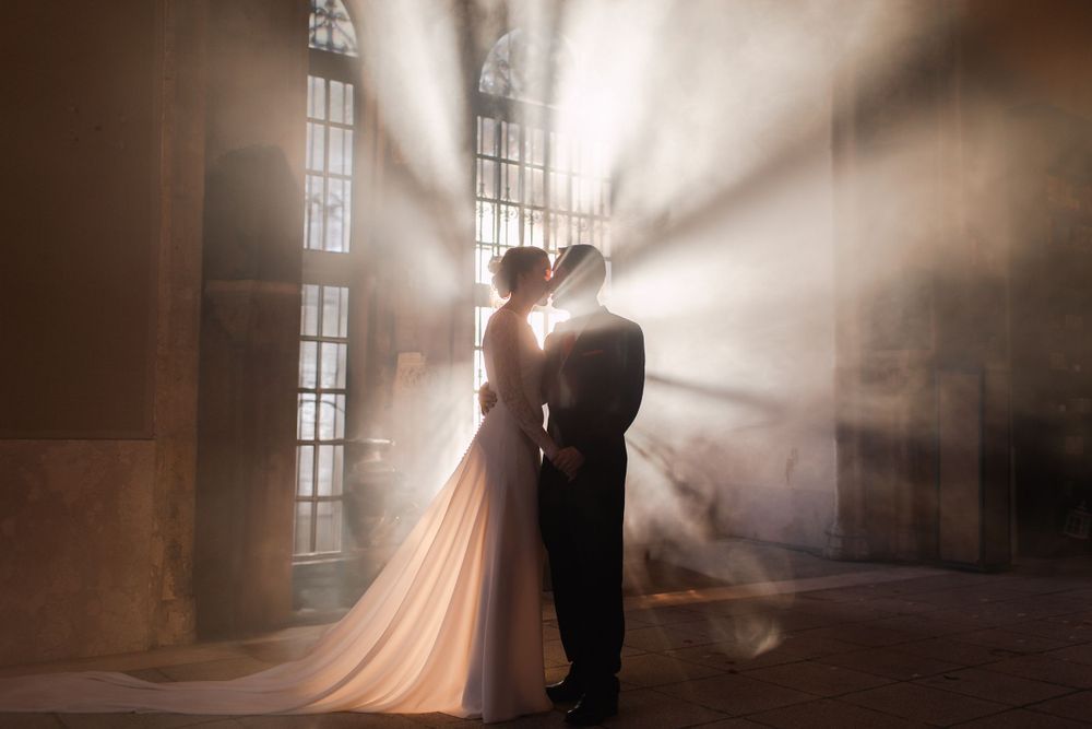 Una pareja de siluetas se abraza en una iglesia iluminada por el sol mientras unos rayos dramáticos entran por las ventanas creando una atmó
