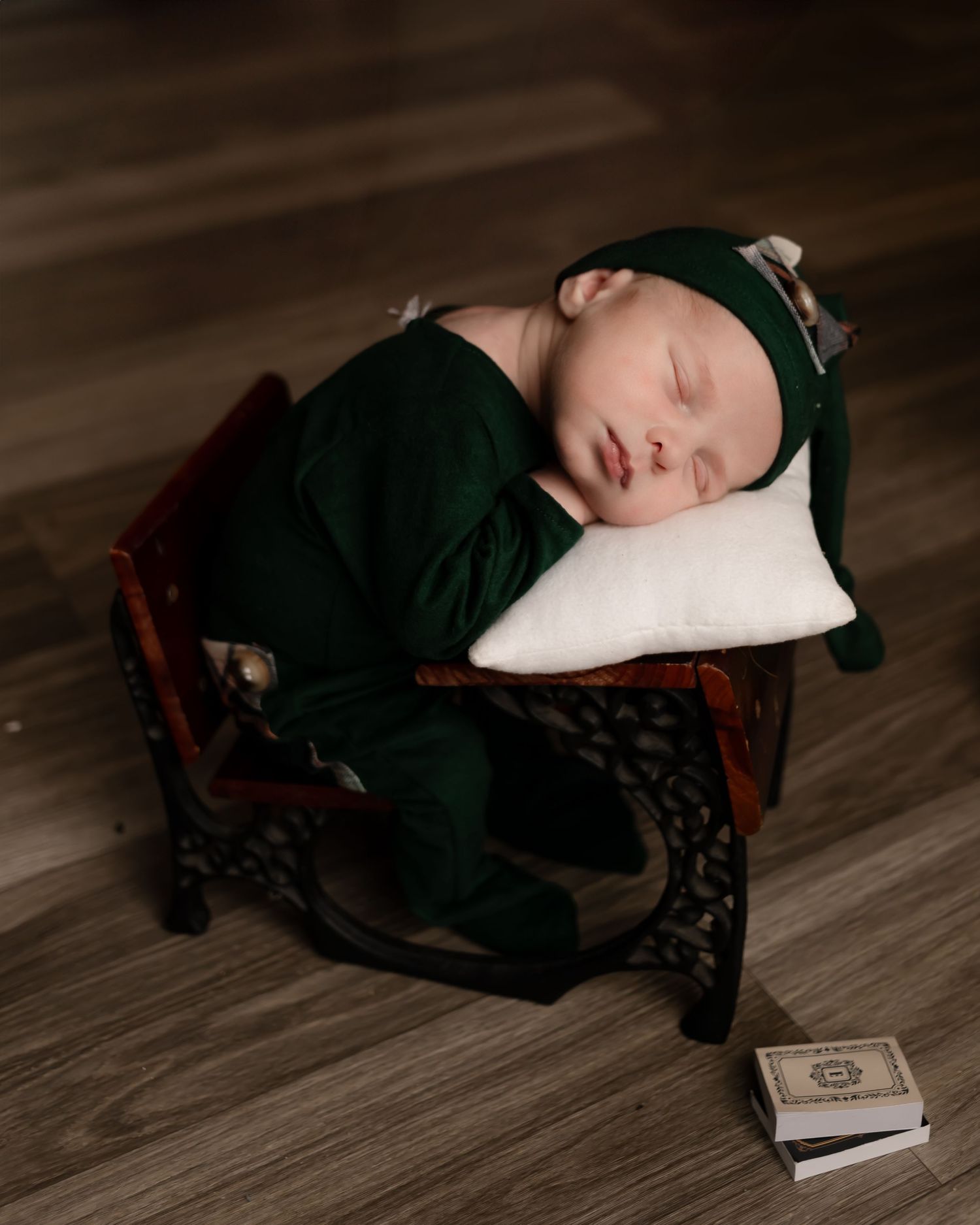 Sleeping baby in green outfit nestled on vintage wood chair.