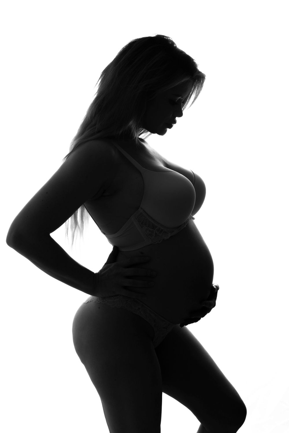 Artistic black and white silhouette of a pregnant woman in profile with hand on hip against white background.