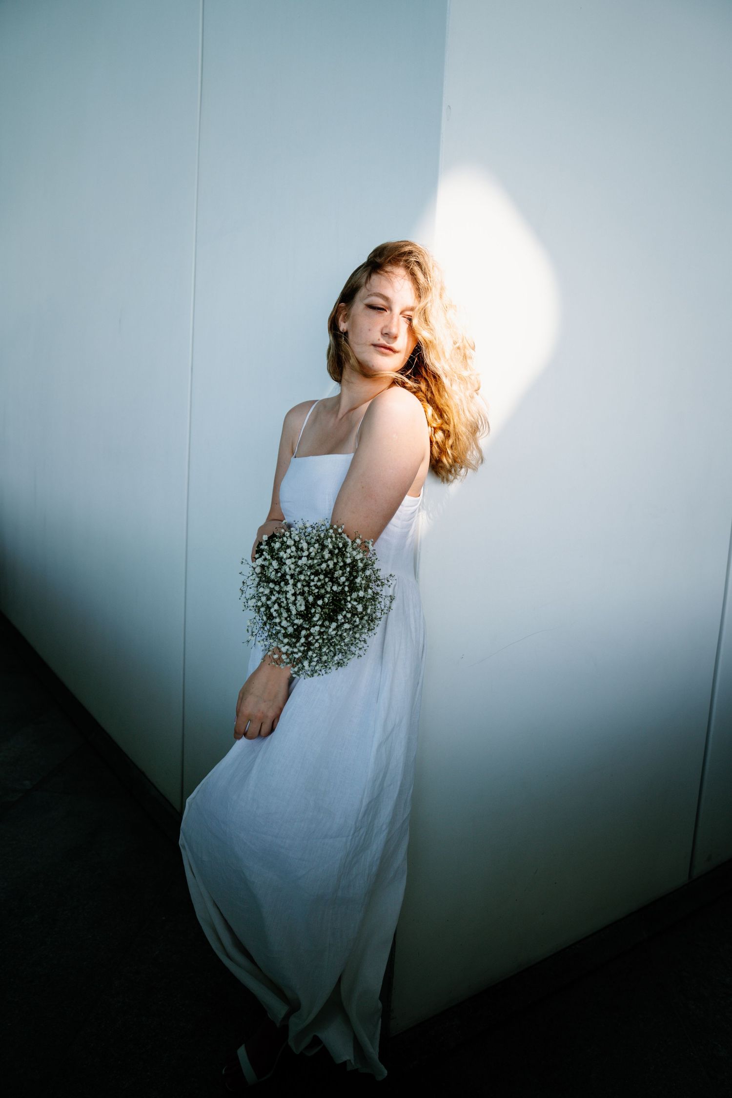 A woman in a flowing white dress holding baby's breath flowers against a minimalist background.