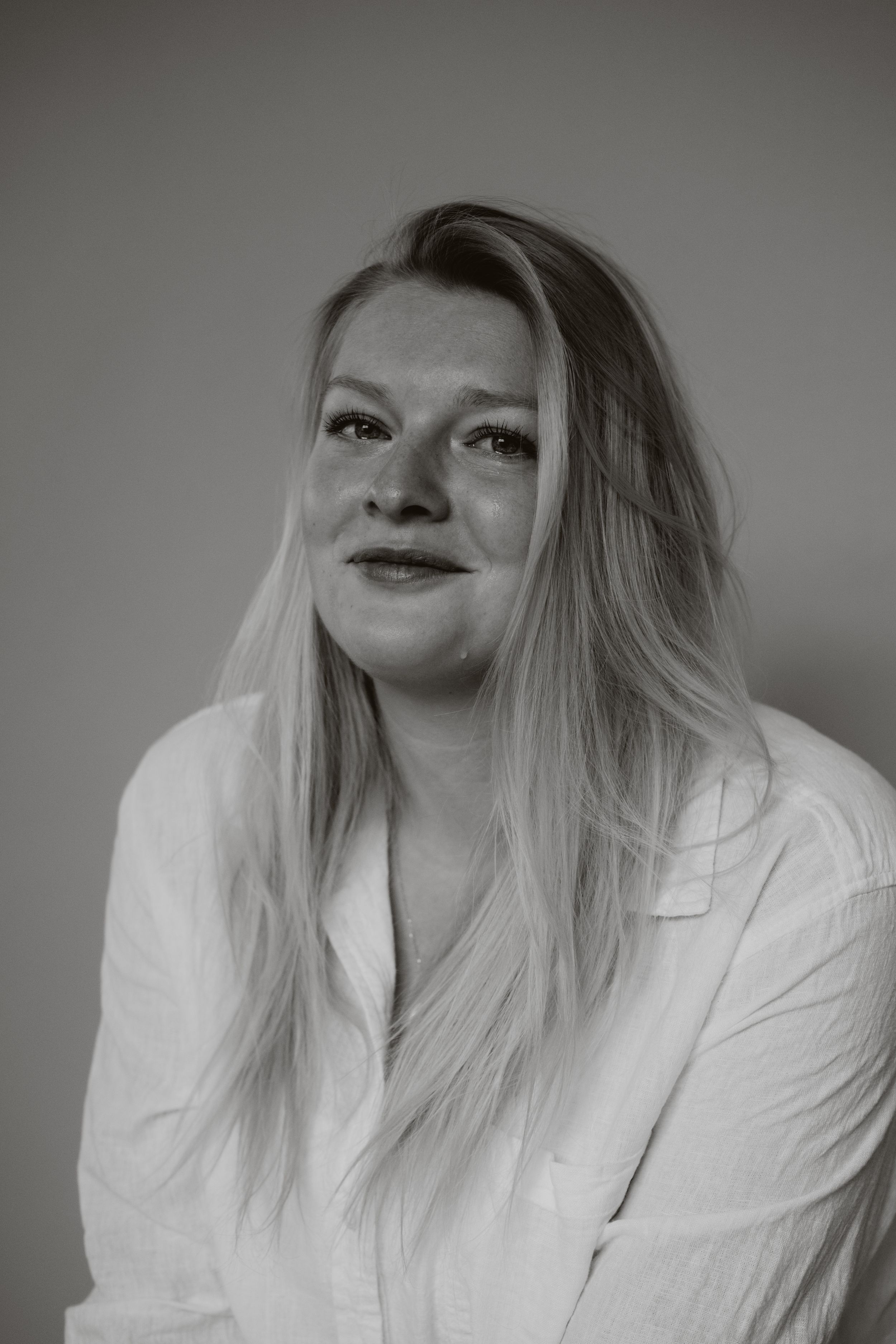 Black and white portrait of a smiling blonde woman in a white blazer.