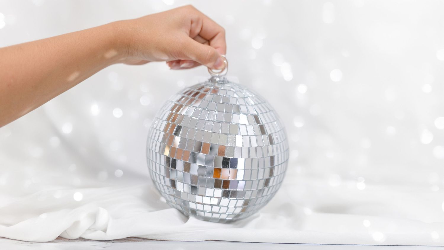 Hand holding a sparkling disco ball creating reflective light patterns on white background. Perth WA Photo booth Hire Event Booth
