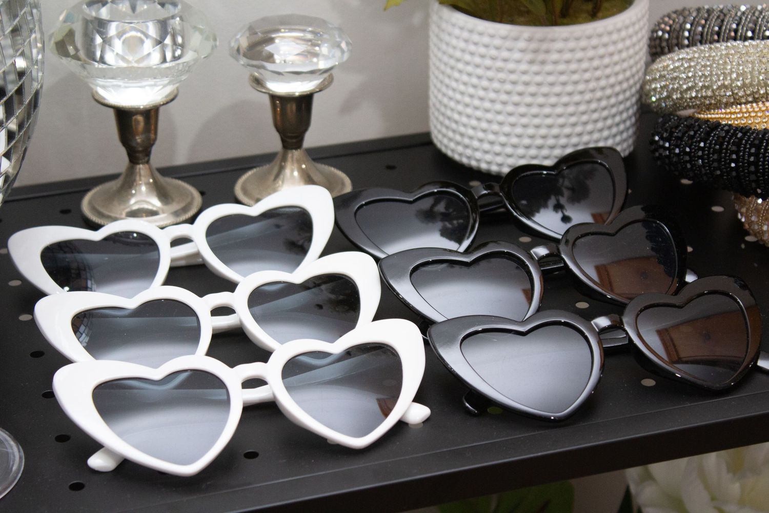 Collection of trendy heart-shaped sunglasses in white and black frames displayed on a dark surface. Perth WA Photo booth Hire Event Booth