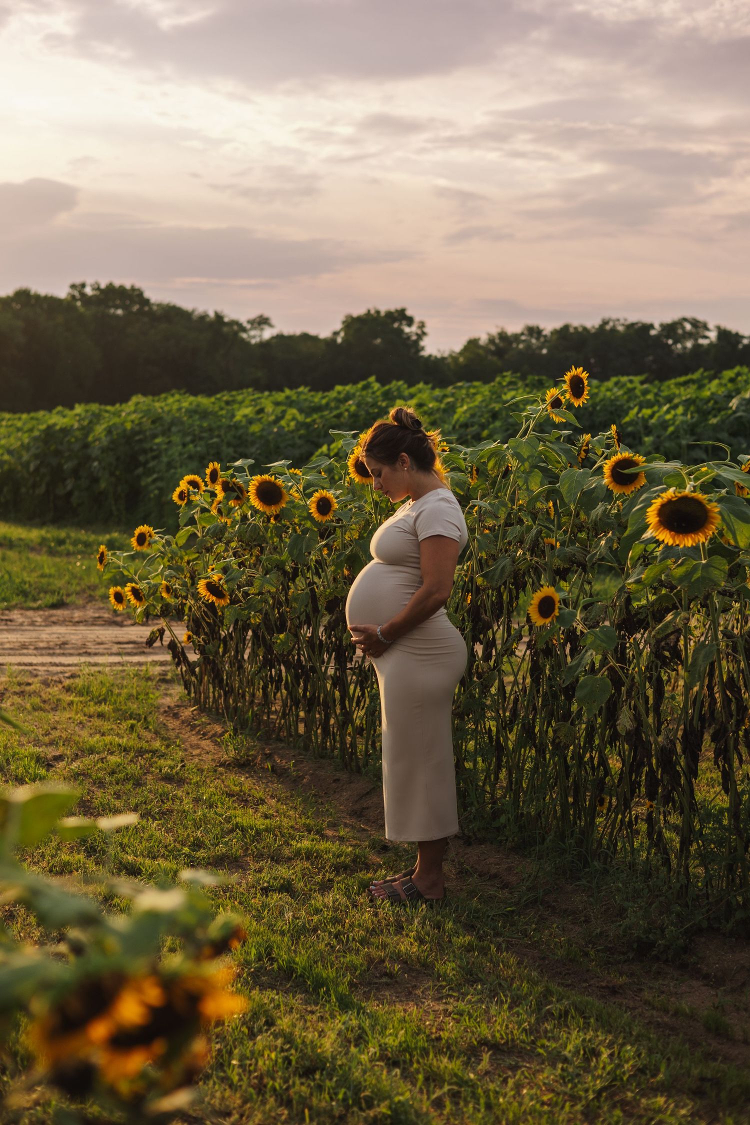 Person in white dress poses near large tree during golden hour in grassy field.