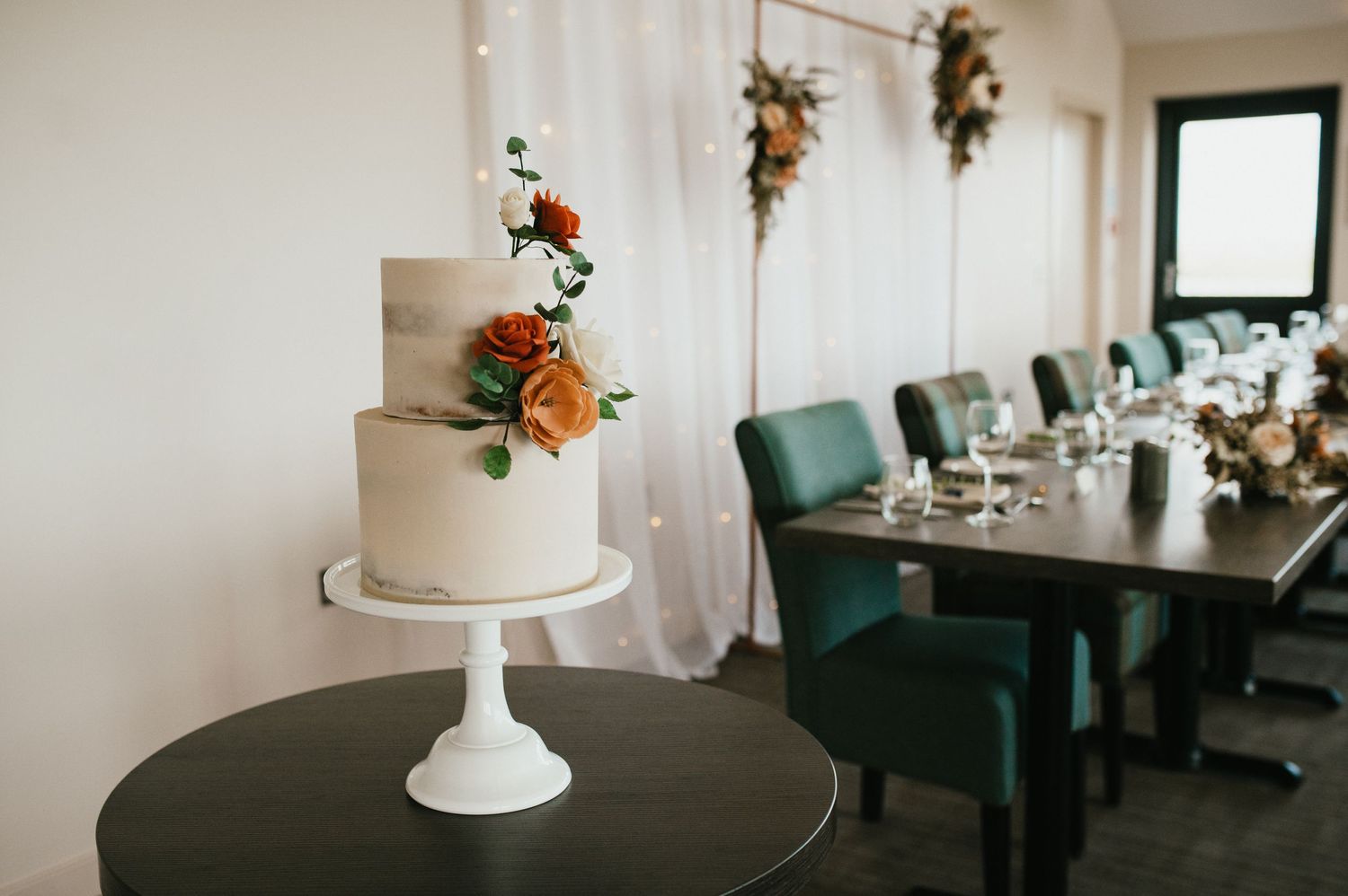 Simple white tiered cake with orange floral accents on black pedestal.