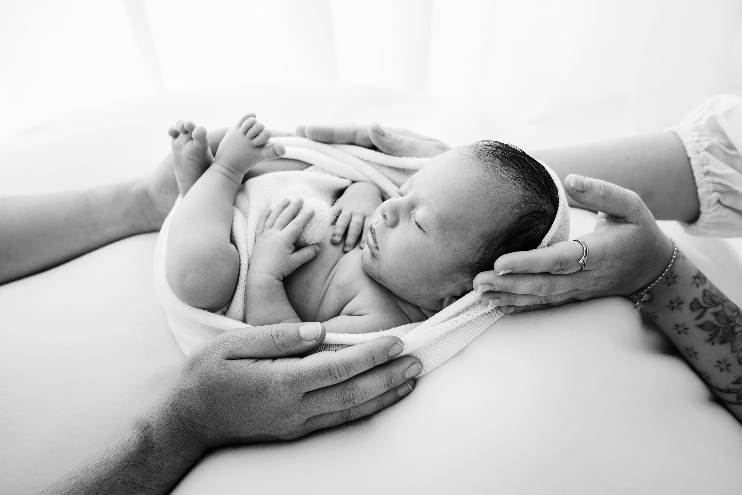 Black and white portrait of sleeping newborn baby being cradled by gentle hands.