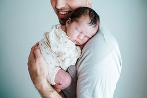 Intimate lifestyle newborn session with baby being cradled in soft lighting.