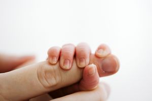 Macro shot of tiny newborn baby fingers being held by adult hand.