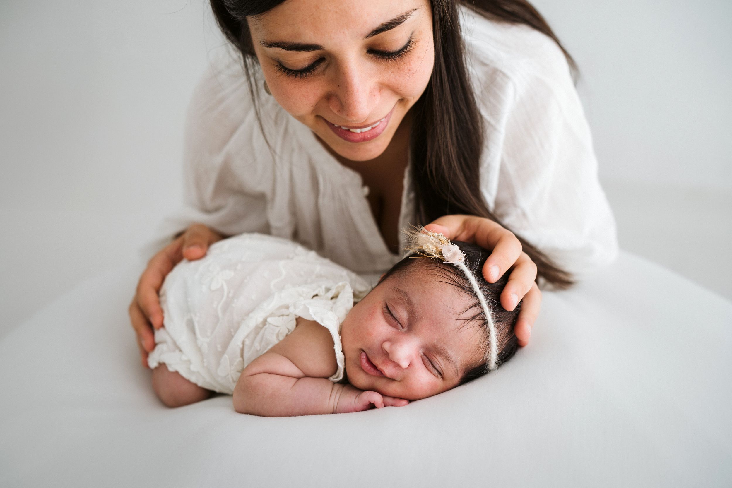 Intimate newborn photography session with parent and baby on white background.