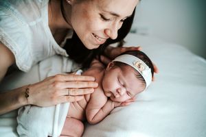 Tender newborn photography session showing baby being held on white bedding.