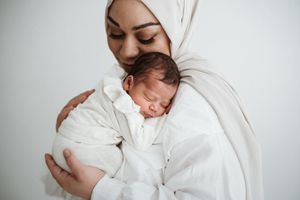 Family wearing white clothing cuddles together in minimalist studio setting.