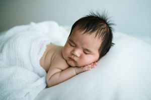 Close-up portrait of sleeping newborn baby on white bedding.