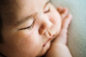 Close-up portrait of a sleeping newborn baby's face against a light background.
