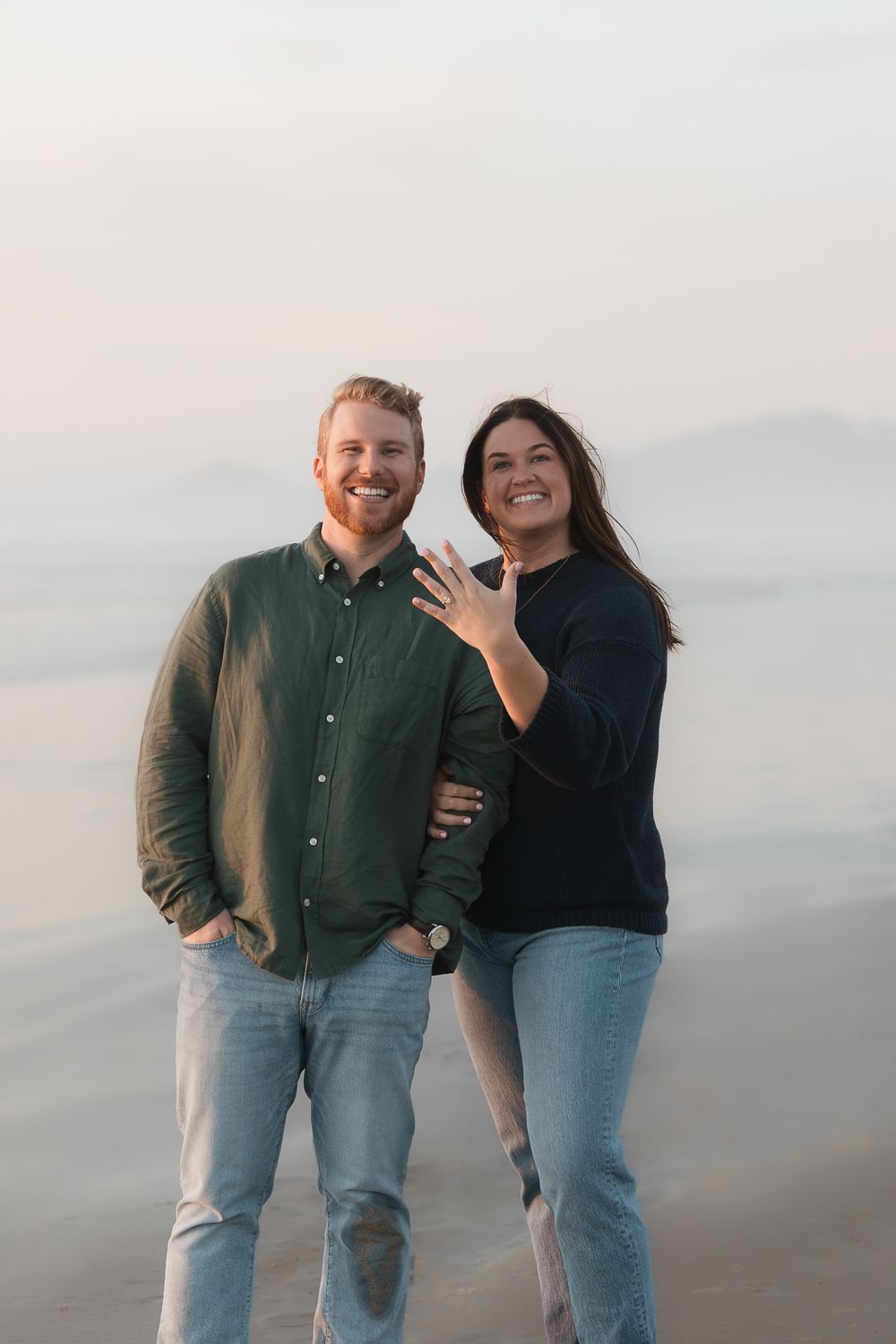 Happy couple celebrating their engagement on a misty beach.