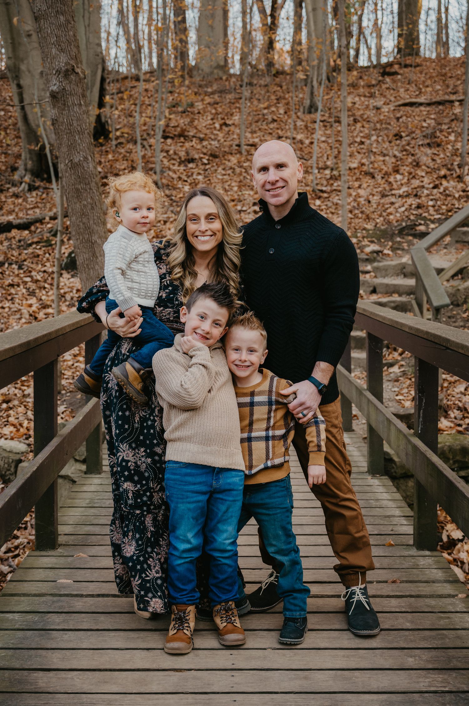 A happy family of five poses together on a wooden bridge surrounded by fall foliage.