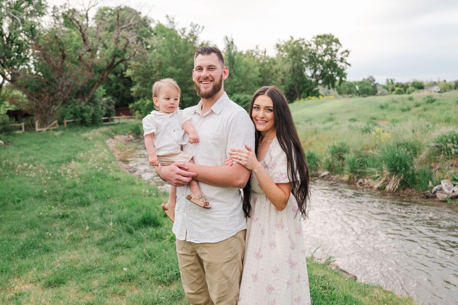 Family of three poses together by a creek in a natural outdoor setting.