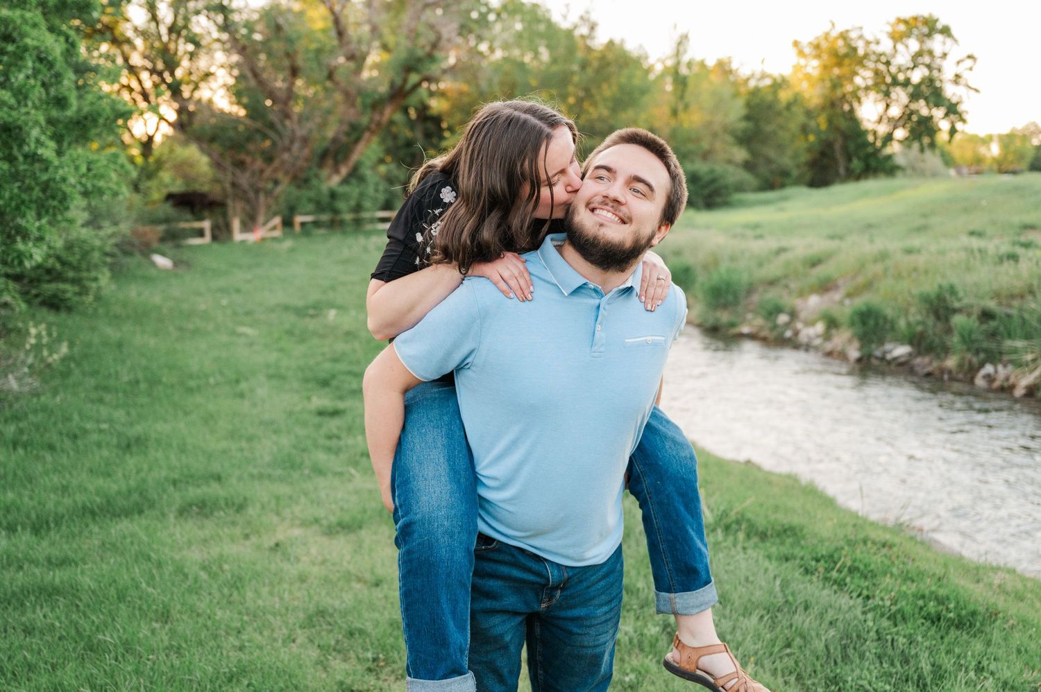 Playful couple enjoying a piggyback ride in a scenic outdoor setting with lush greenery.