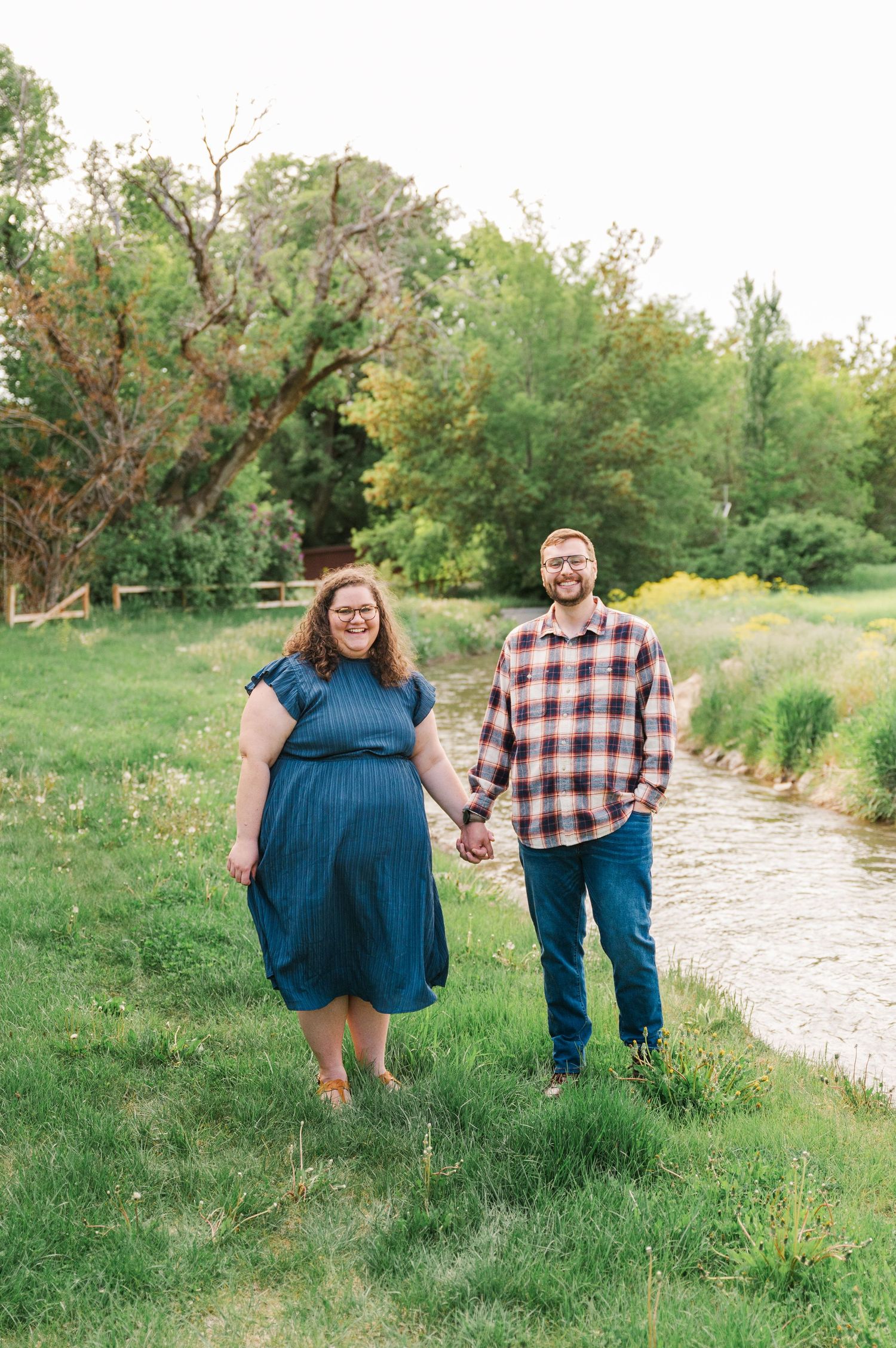 Couple holding hands while standing by a scenic creek on a spring day.