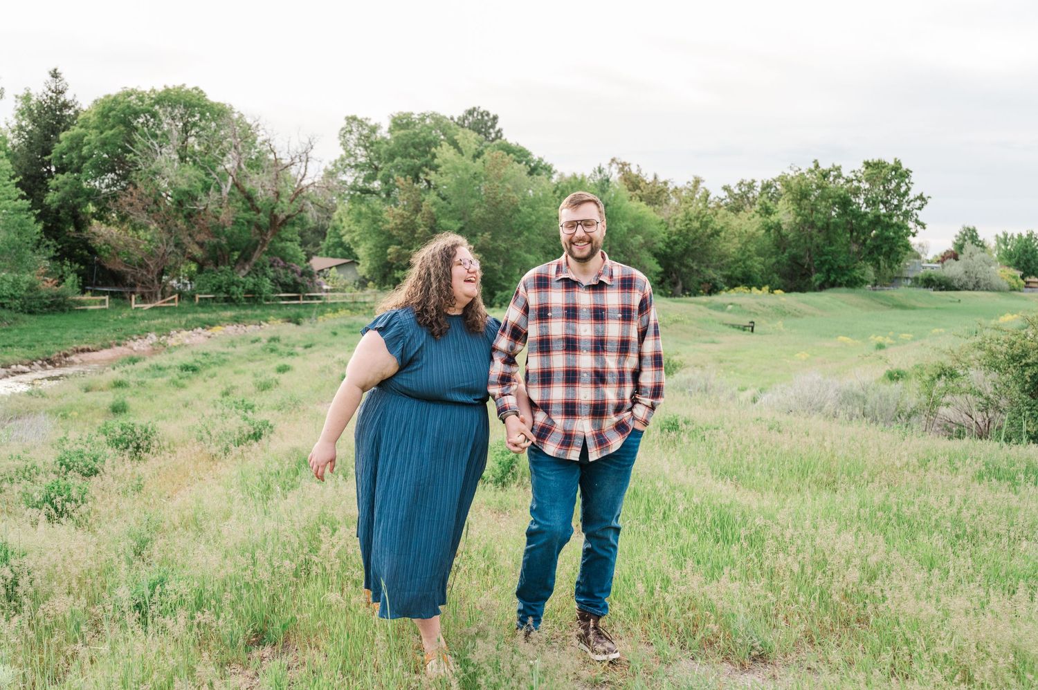 A couple walks together through a grassy meadow on a sunny day.