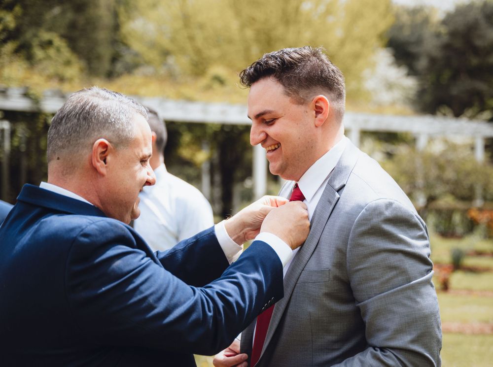 Formal moment of tie adjustment between two people at an outdoor event.