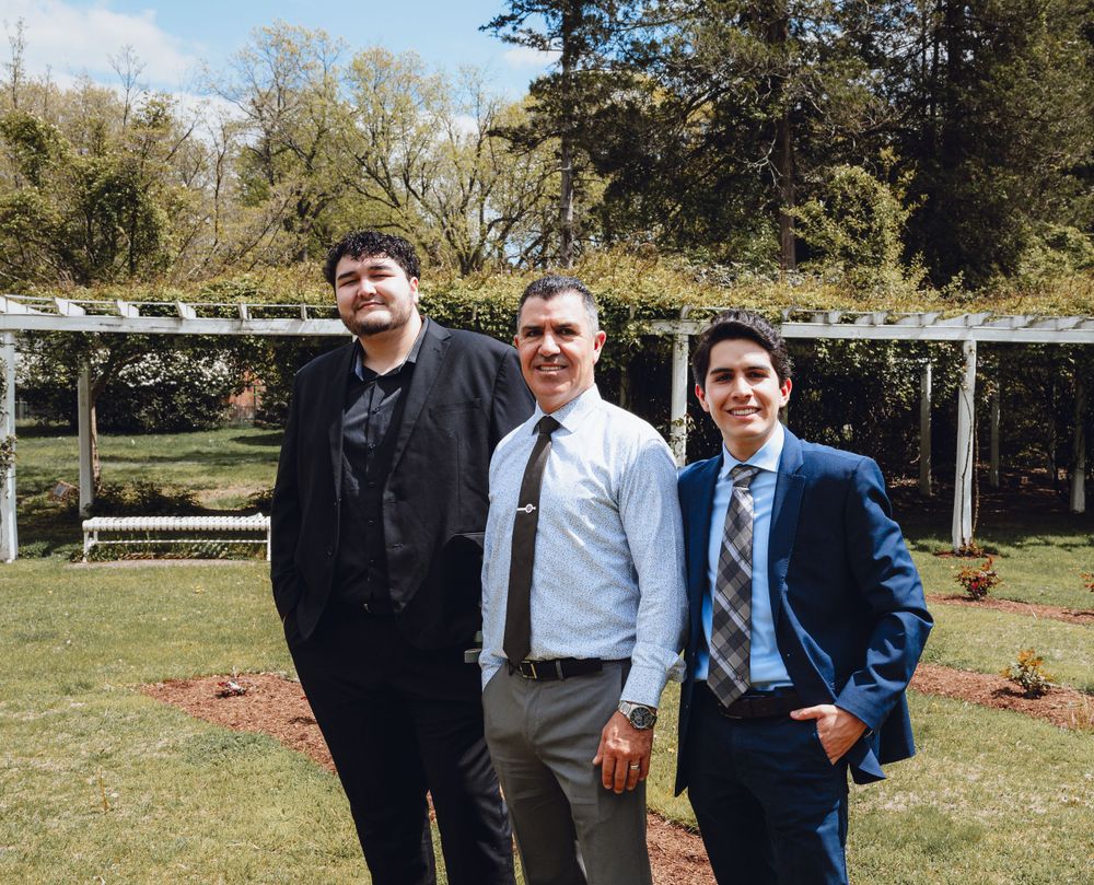 Three formally dressed people standing together outdoors for a group photo.