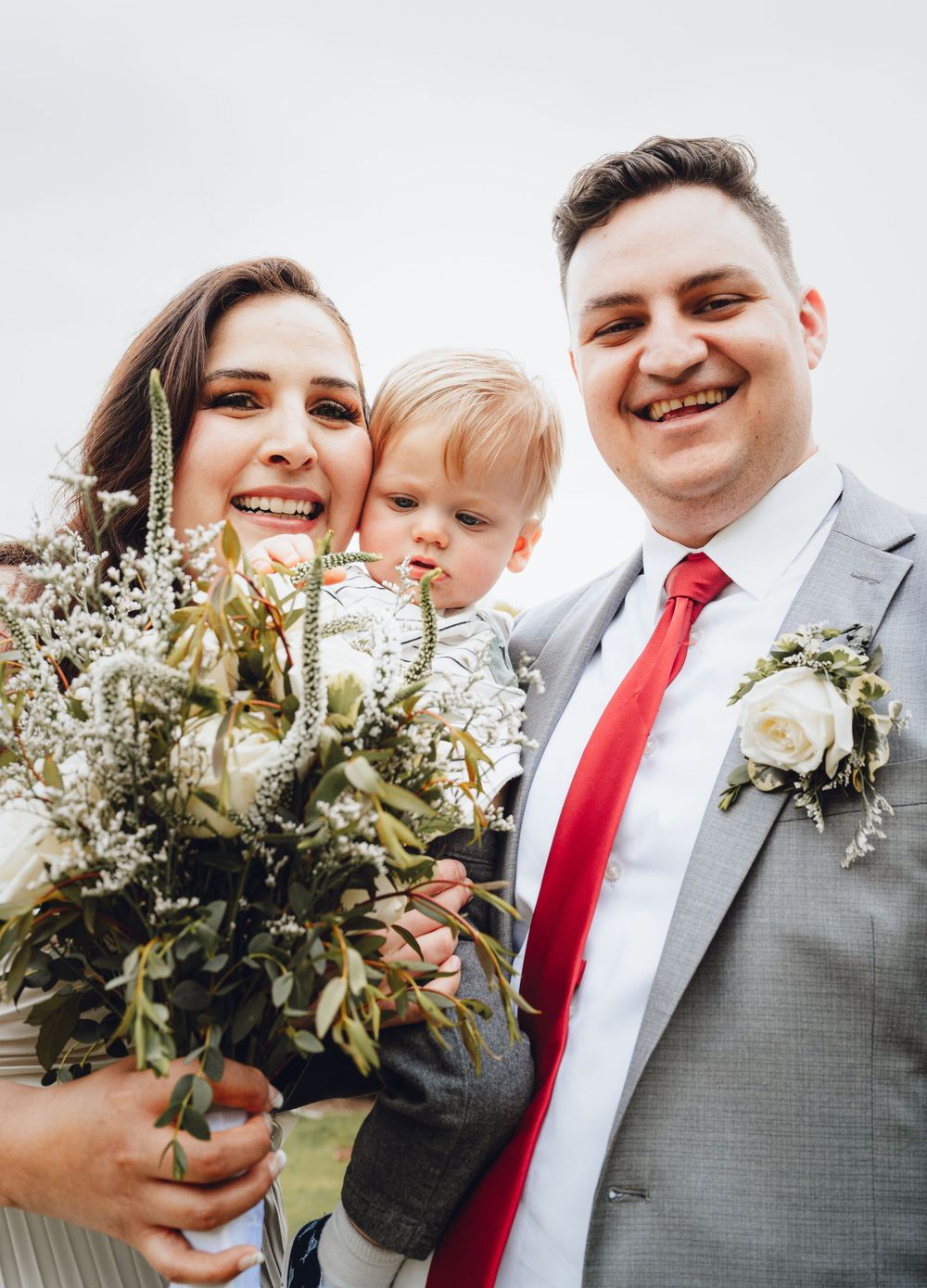 A joyful family moment with wedding bouquet and baby outdoors.