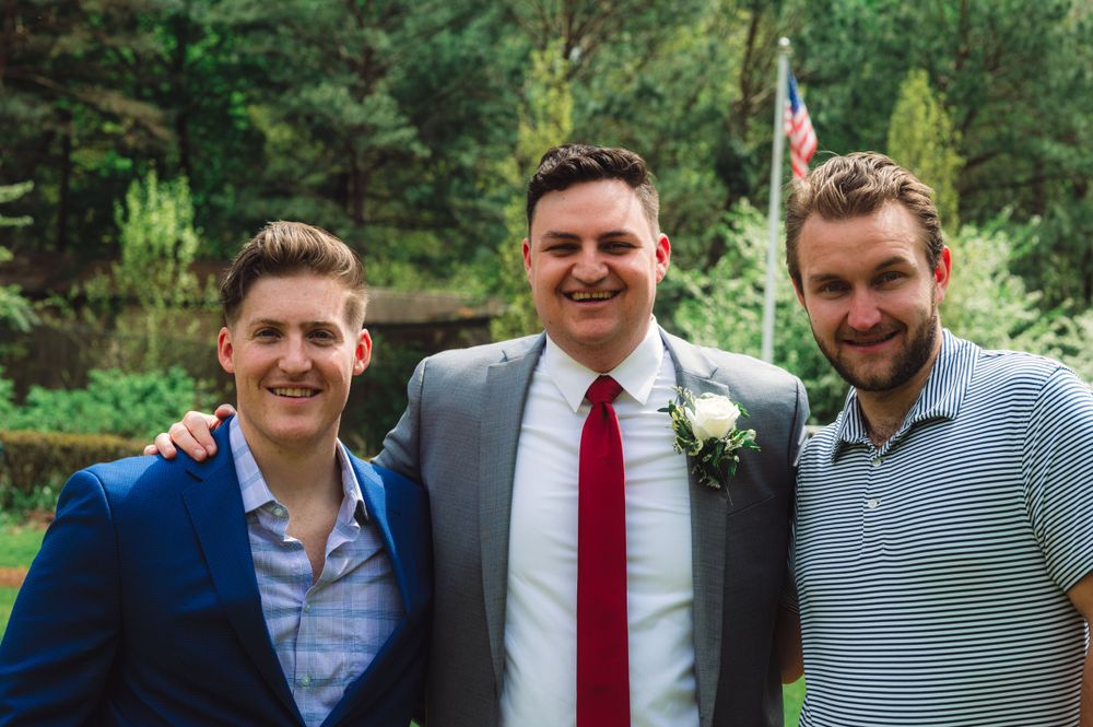 Three friends in formal and casual attire pose together outdoors.